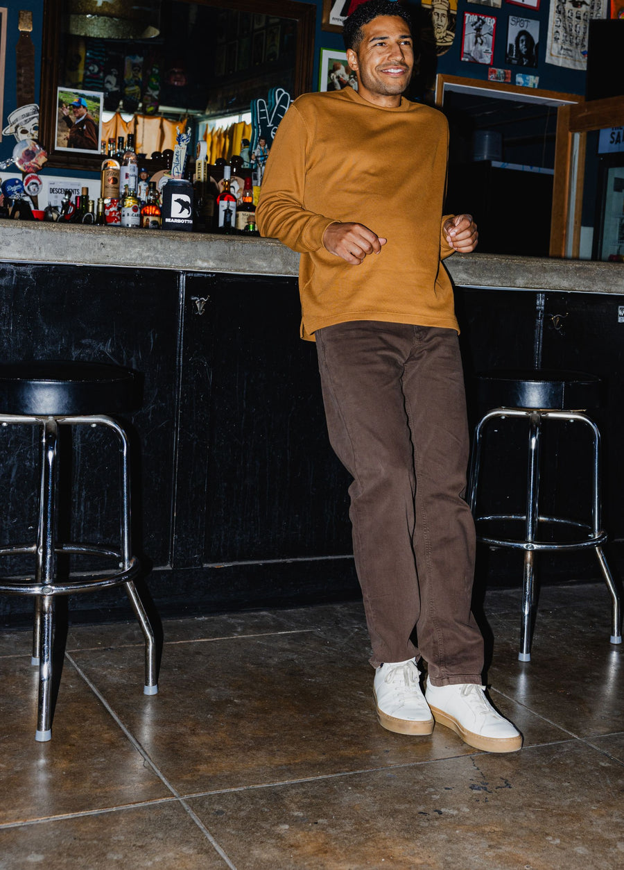 Man standing in a bar wearing Thermal Knit Crew in Cider and Stretch Travel Jeans in Cocoa.