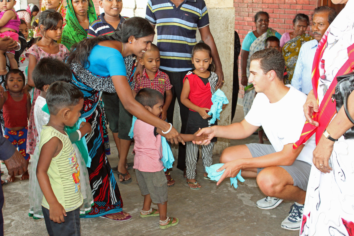 CEO Robert Felder shaking a boys hand in a group of people who is holding a pair of blue shorts donated by Bearbottom in Bangladesh