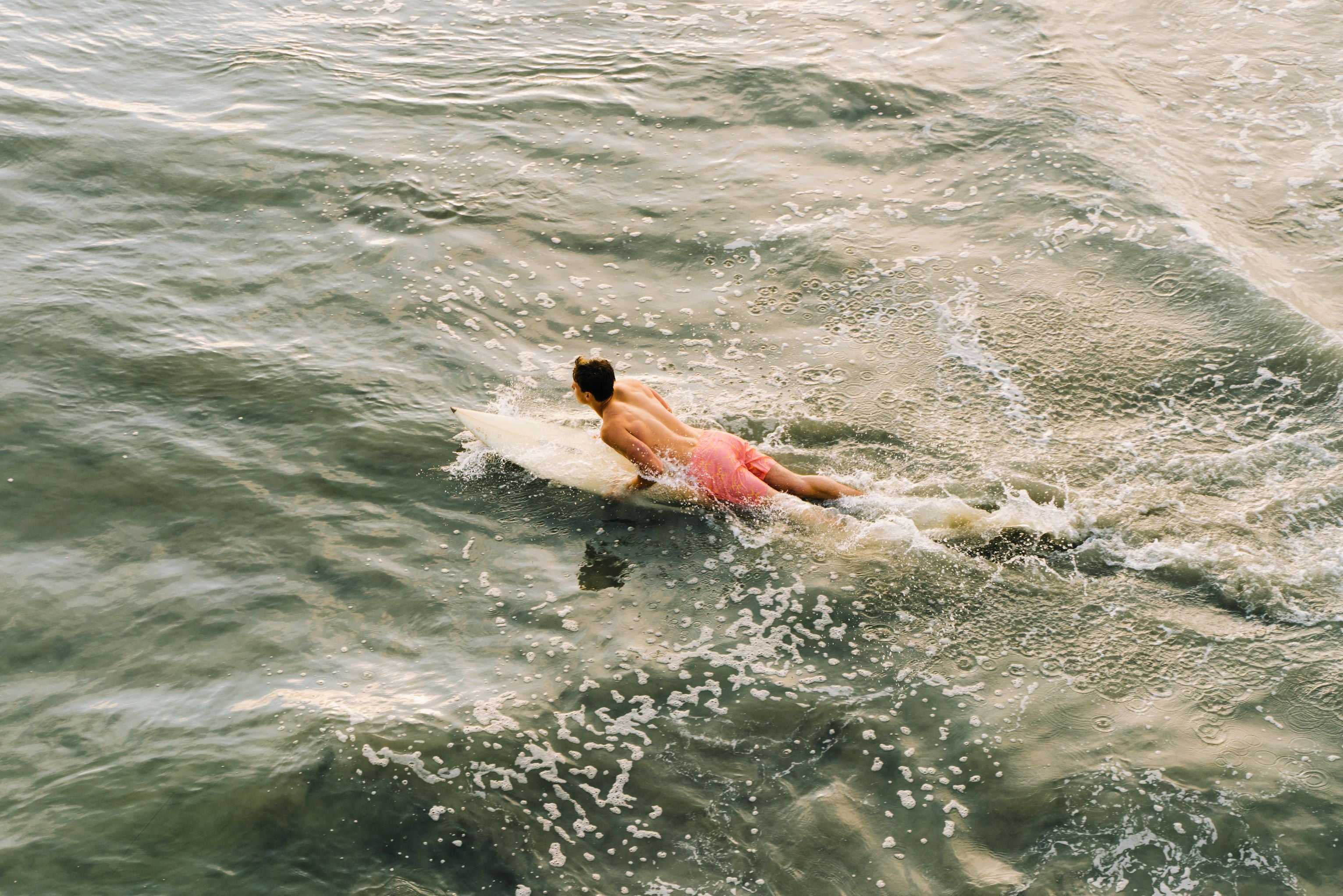 Man laying on surf board in ocean wearing Stretch Swim 5.5" Groovy