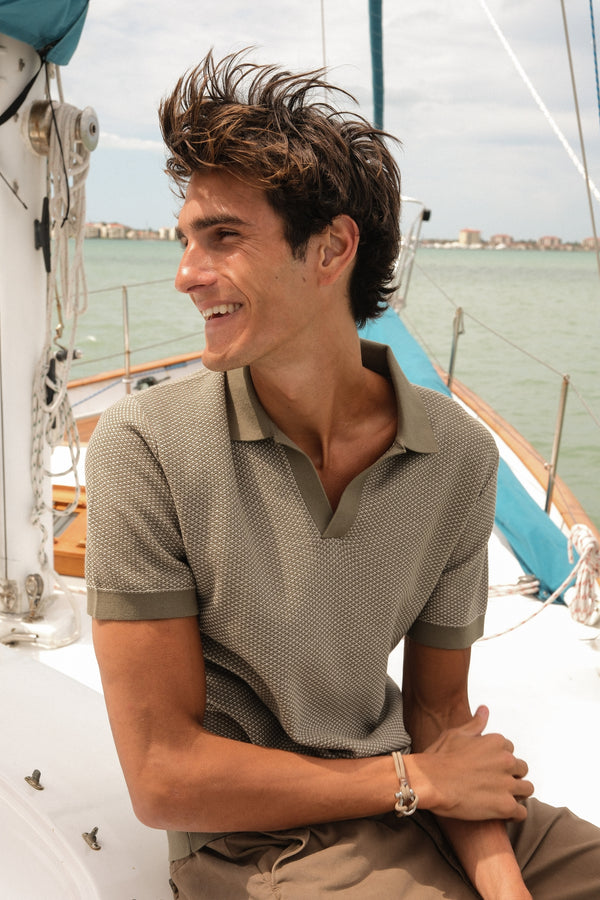 Model in the Honeycomb Sweater Polo in Driftwood, leaning on the rail of a sailboat