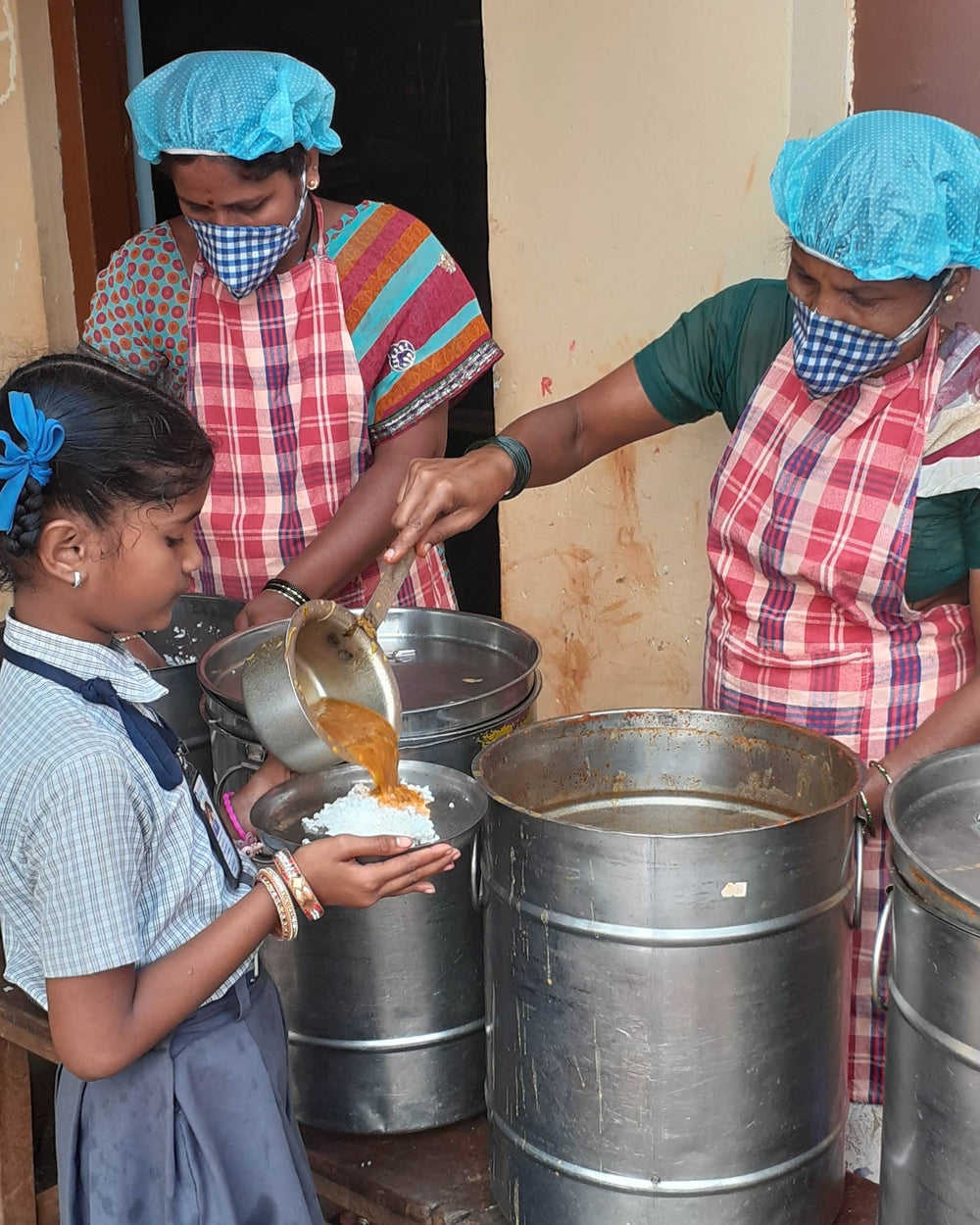 Children holding plates as school meals are served from large pots