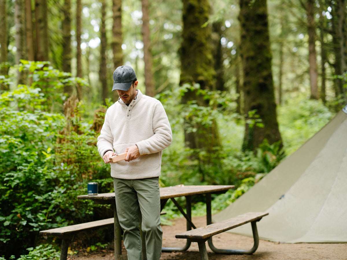 A man by a campfire wearing the Quarter Snap Sherpa Pullover in Bone.