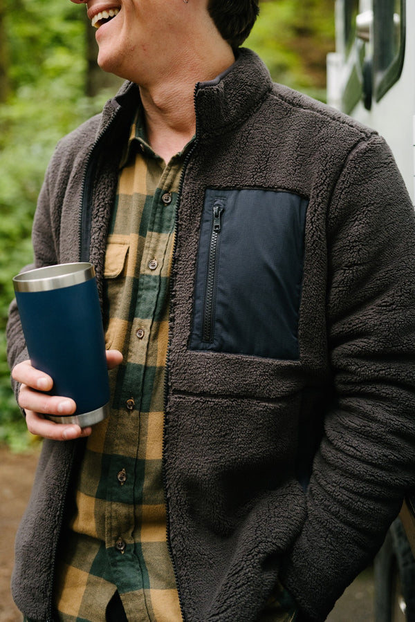 A man outdoors holding a coffee cup wearing the Full Zip Sherpa Jacket in Shadow.