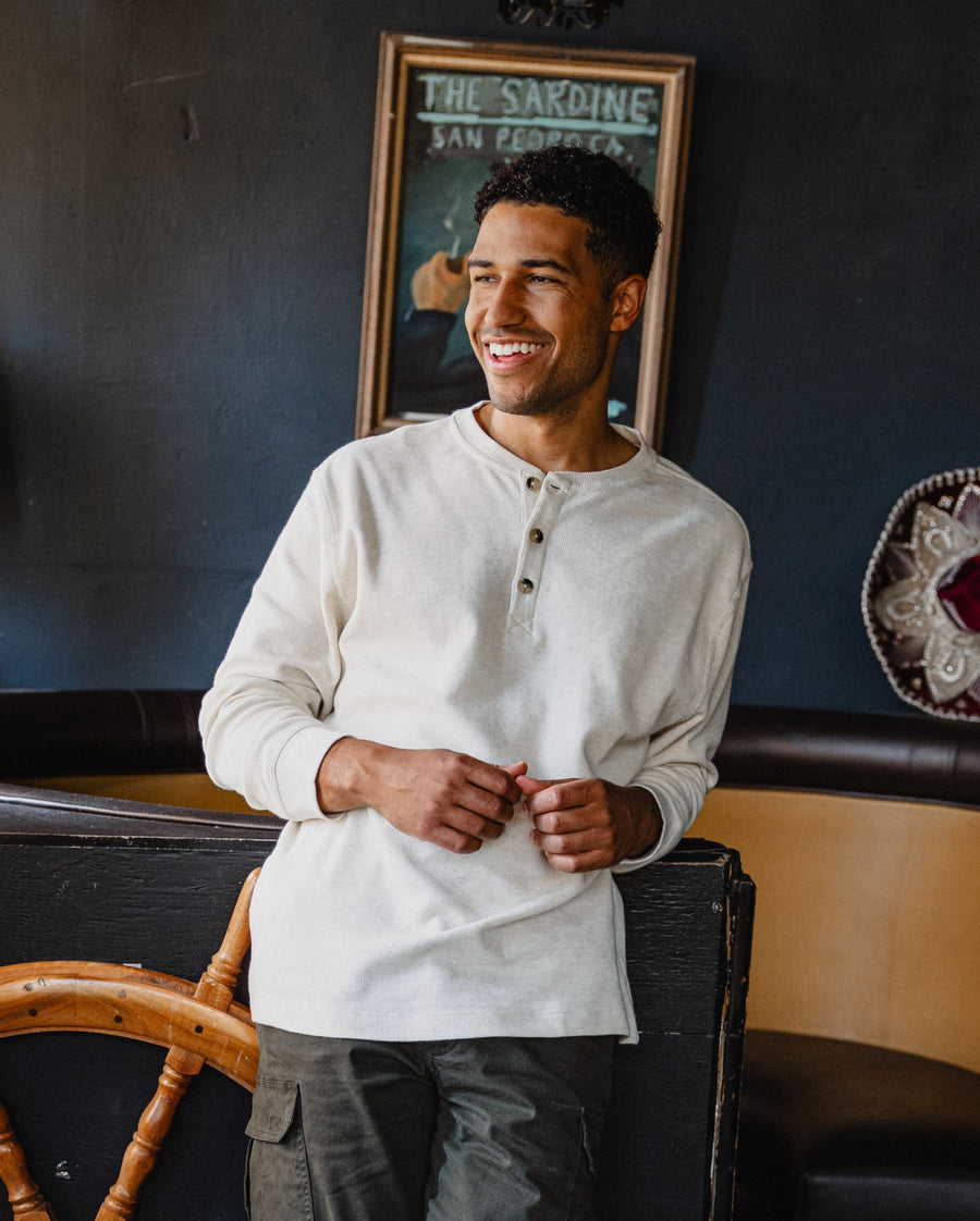 Man wearing a Waffle Knit Henley shirt in stone standing in a room with dark walls and wooden furniture.