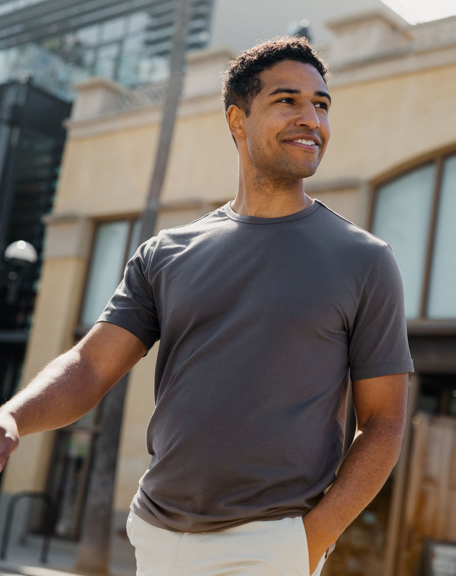 Man wearing Supima Tee in Shadow standing outdoors with a building in the background
