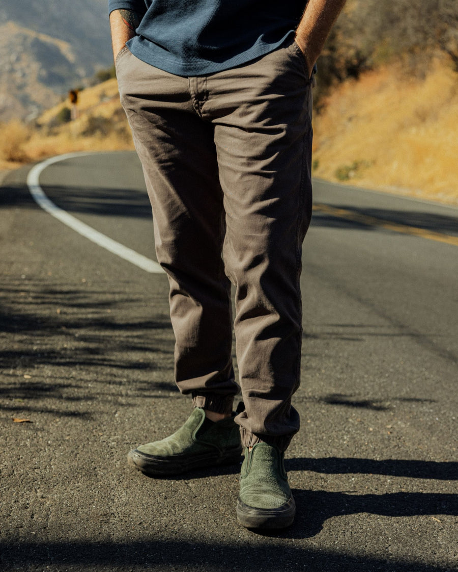 Person wearing stretch jogger pants in bark and green shoes standing on a road with a scenic background