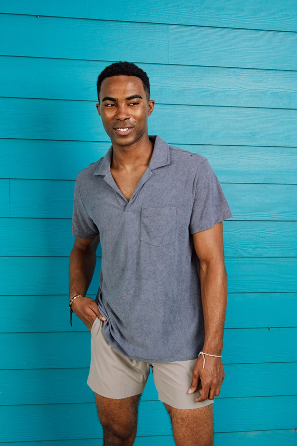 Man standing against an aqua wall in Coastal Terry Polo in Denim and Stretch Swim Solid in Solid Grey