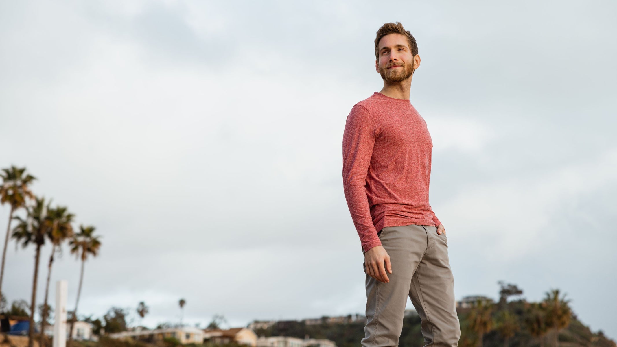 Model standing in California coastline wearing Long Sleeve Tech Tee Rhubarb and Stretch Chino Pants Grey