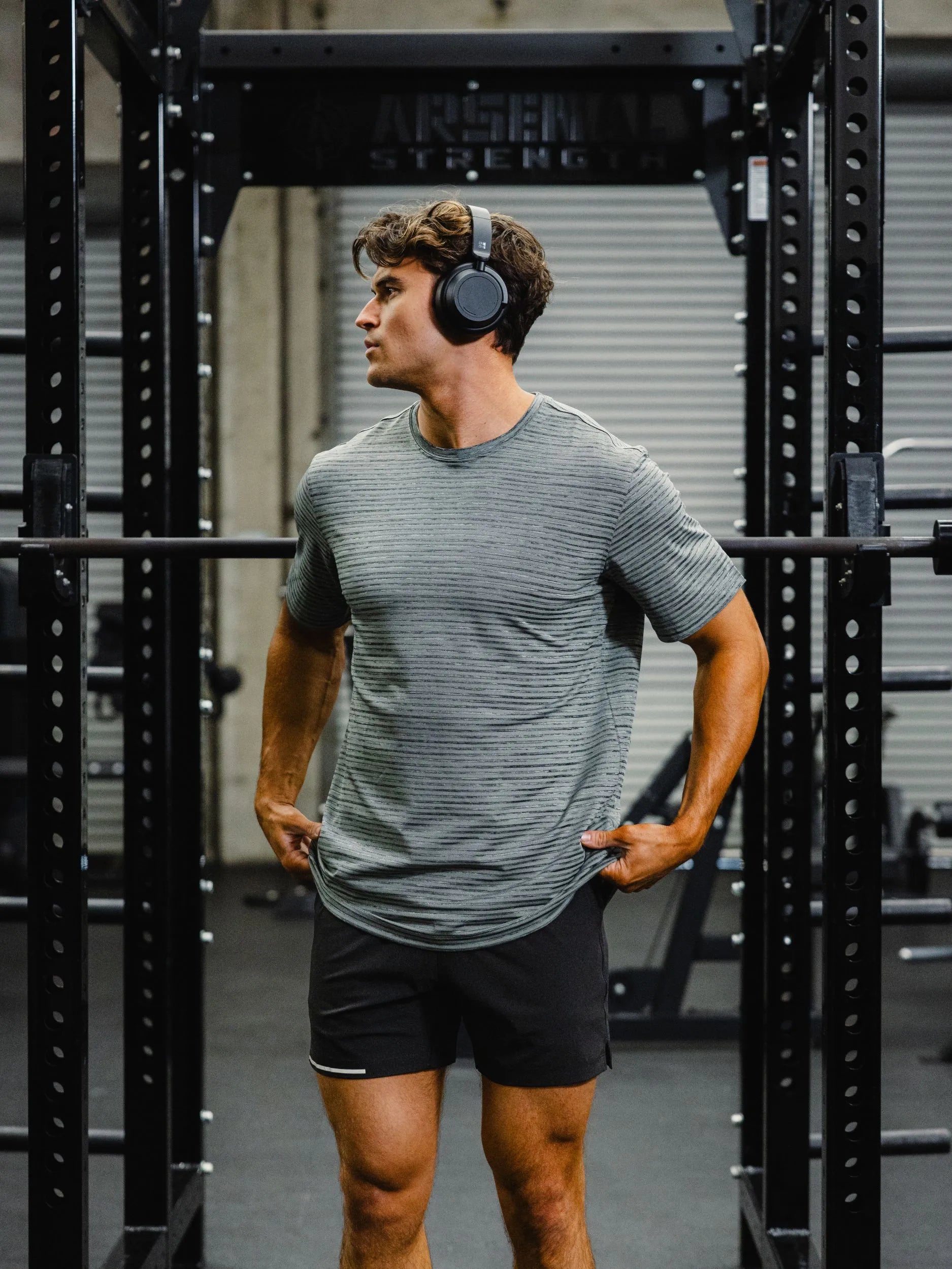 Man wearing headphones and a Stride Shirt in Navy Stripe, Run short v2 in black in a gym setting. Shop Activewear now for top performace.