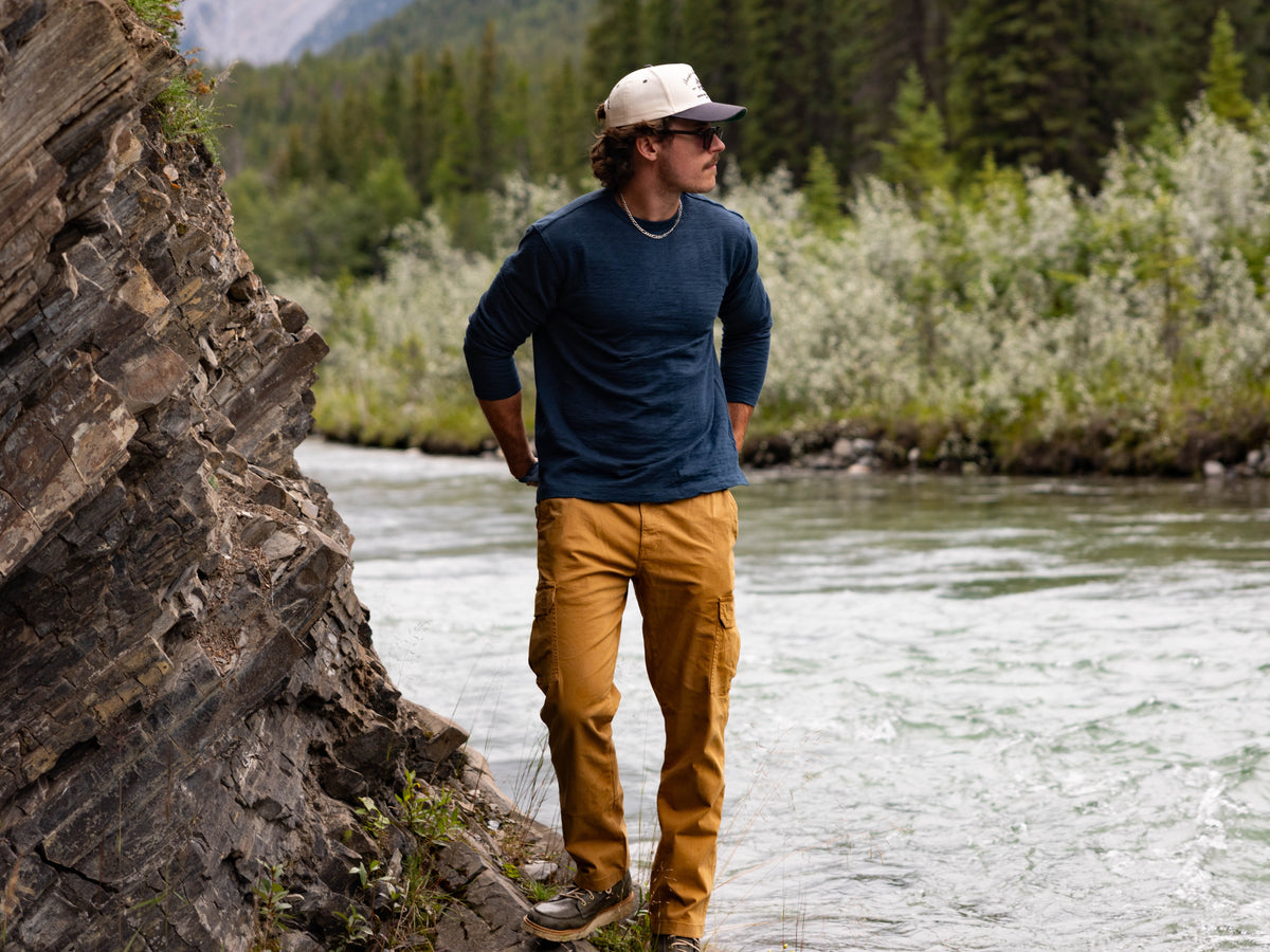 A man standing at the edge of a river in a rocky outdoor setting, wearing the Stretch Cargo Pants and Rugby Crew.