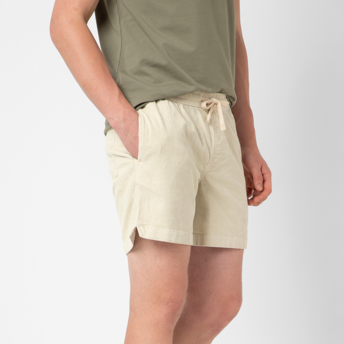 Someone stands against a plain white background wearing a light green t-shirt and Corduroy Easy Short, with one hand in their pocket.