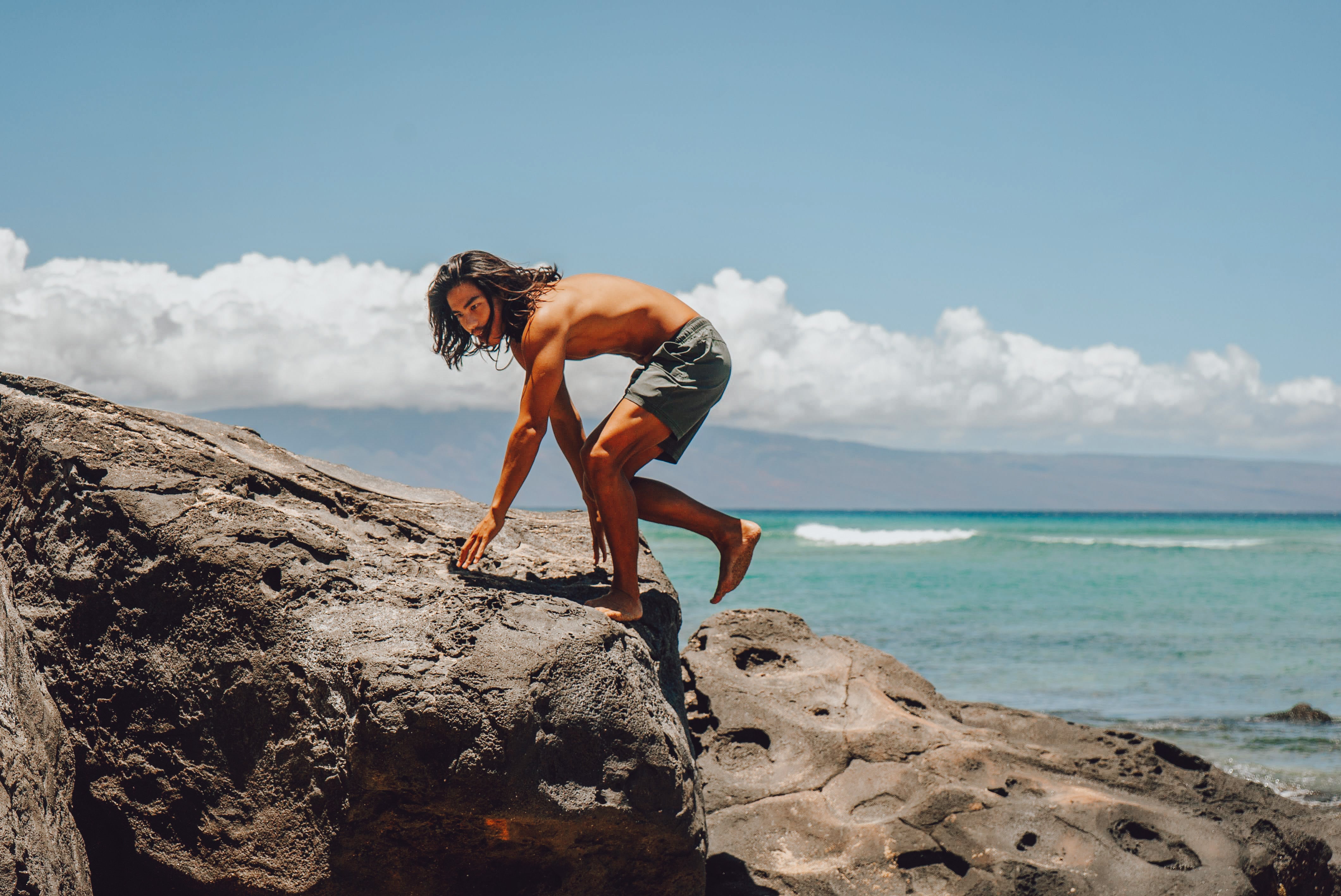 Model climbing on rock by ocean wearing Volley Short 7" Green