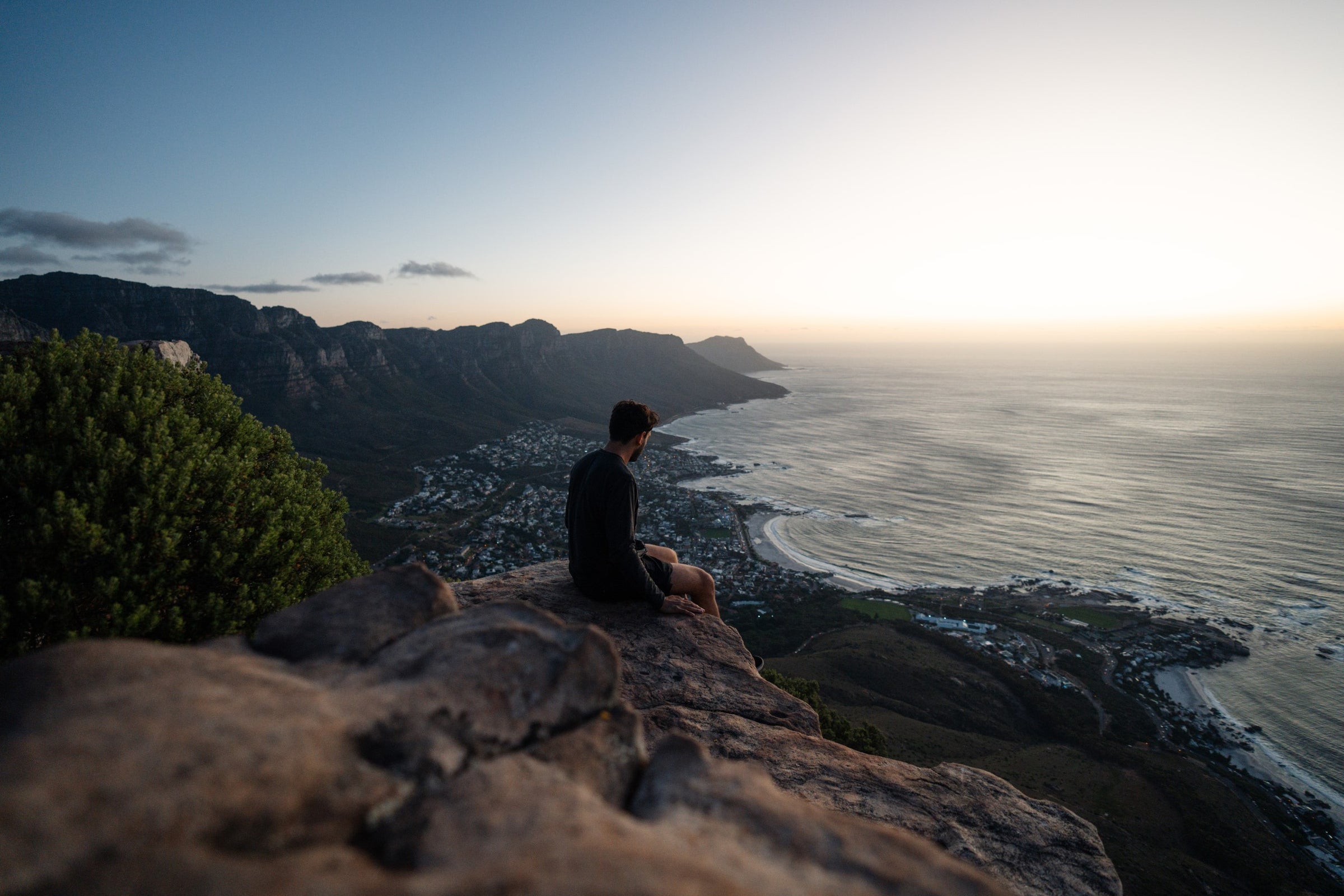 Man sitting on top of a mountain overlooking the ocean