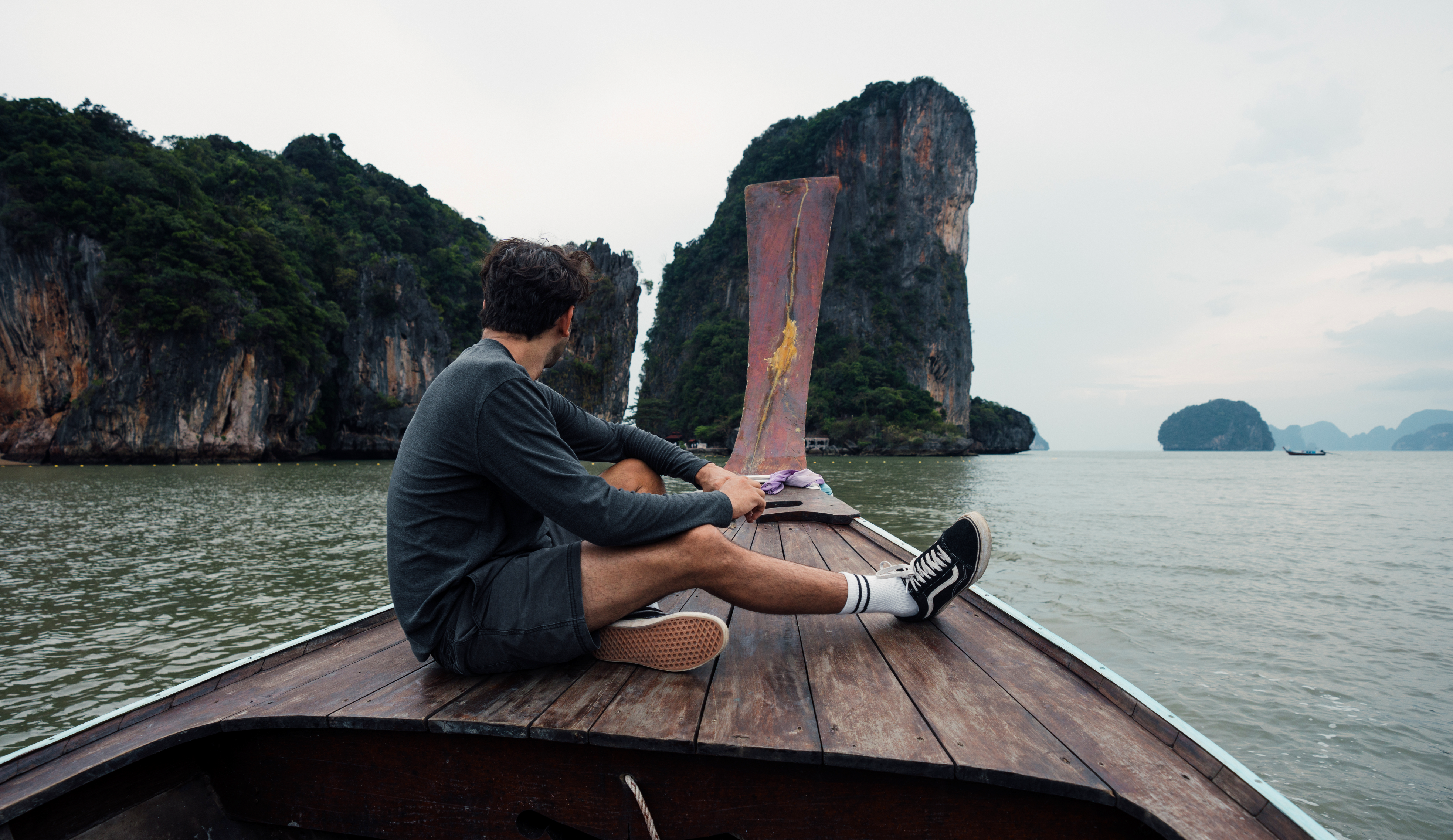 Man wearing Tech Tee Long Sleeve in Charcoal Grey and Volley Short 5.5" in Grey riding on wooden boat in Thailand