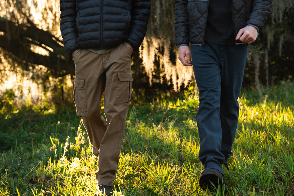 2 men in an outdoor setting walking wearing the Stretch Cargo Pants in Desert and the Stretch Travel Jeans in Navy.