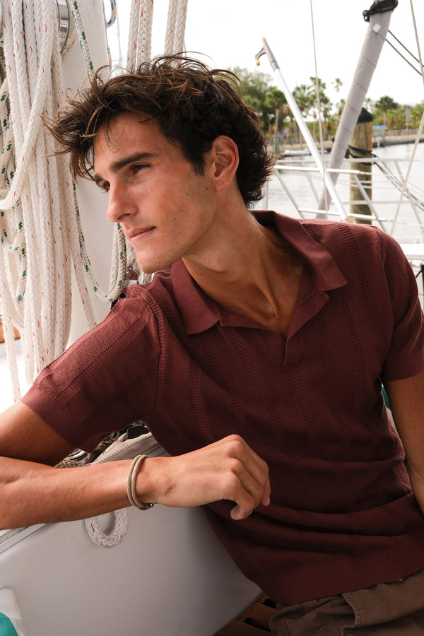 Man wearing the Laddar Knit Sweater Polo in Deep Mauve on a boat