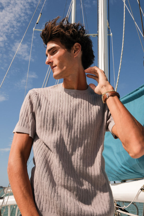Man wearing the Cable Stitch Sweater Crewneck standing on a boat with a clear blue sky background
