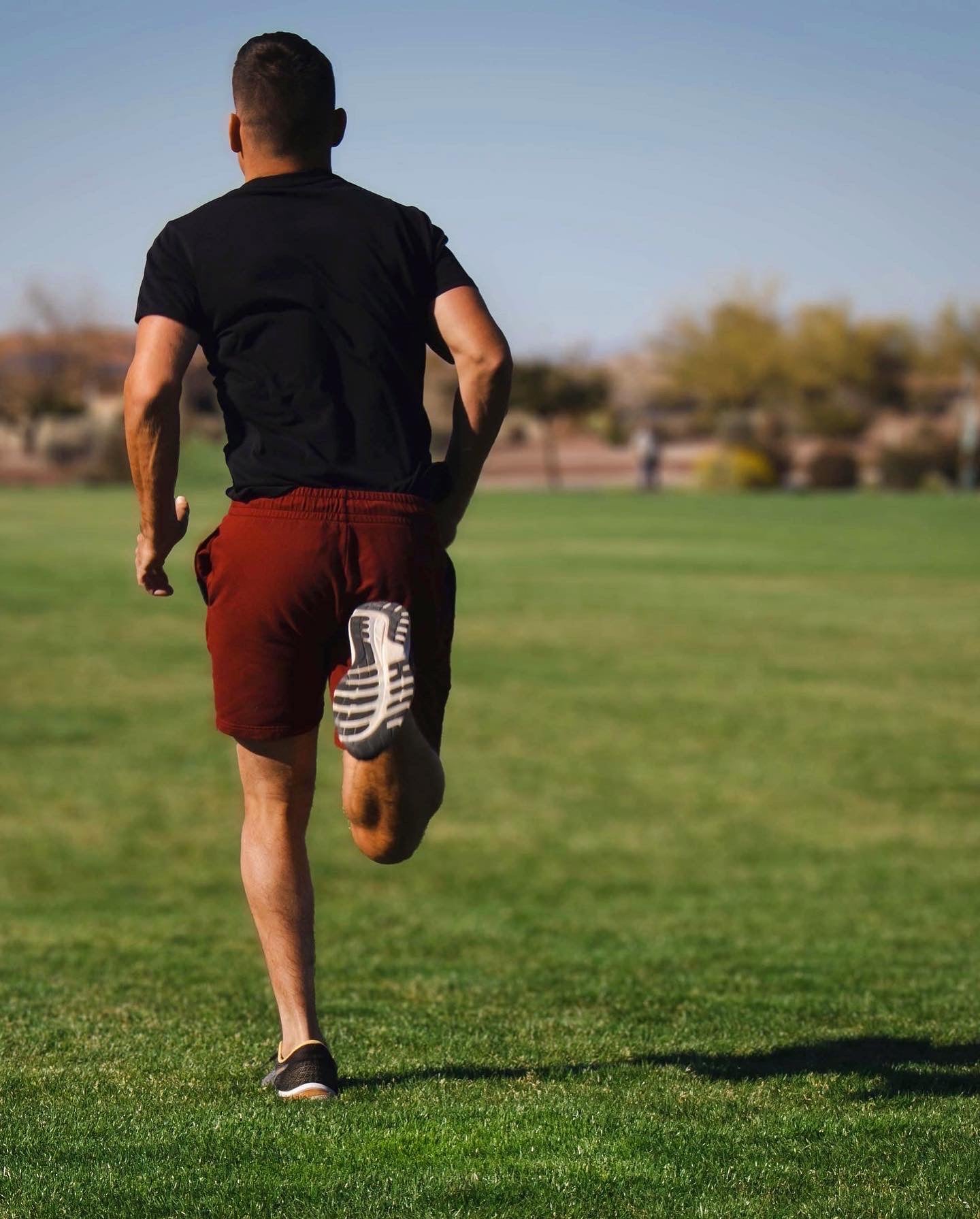 Man running away in grassy field wearing Short Sleeve Tech Tee Solid Black and Loft Short 7" Maroon