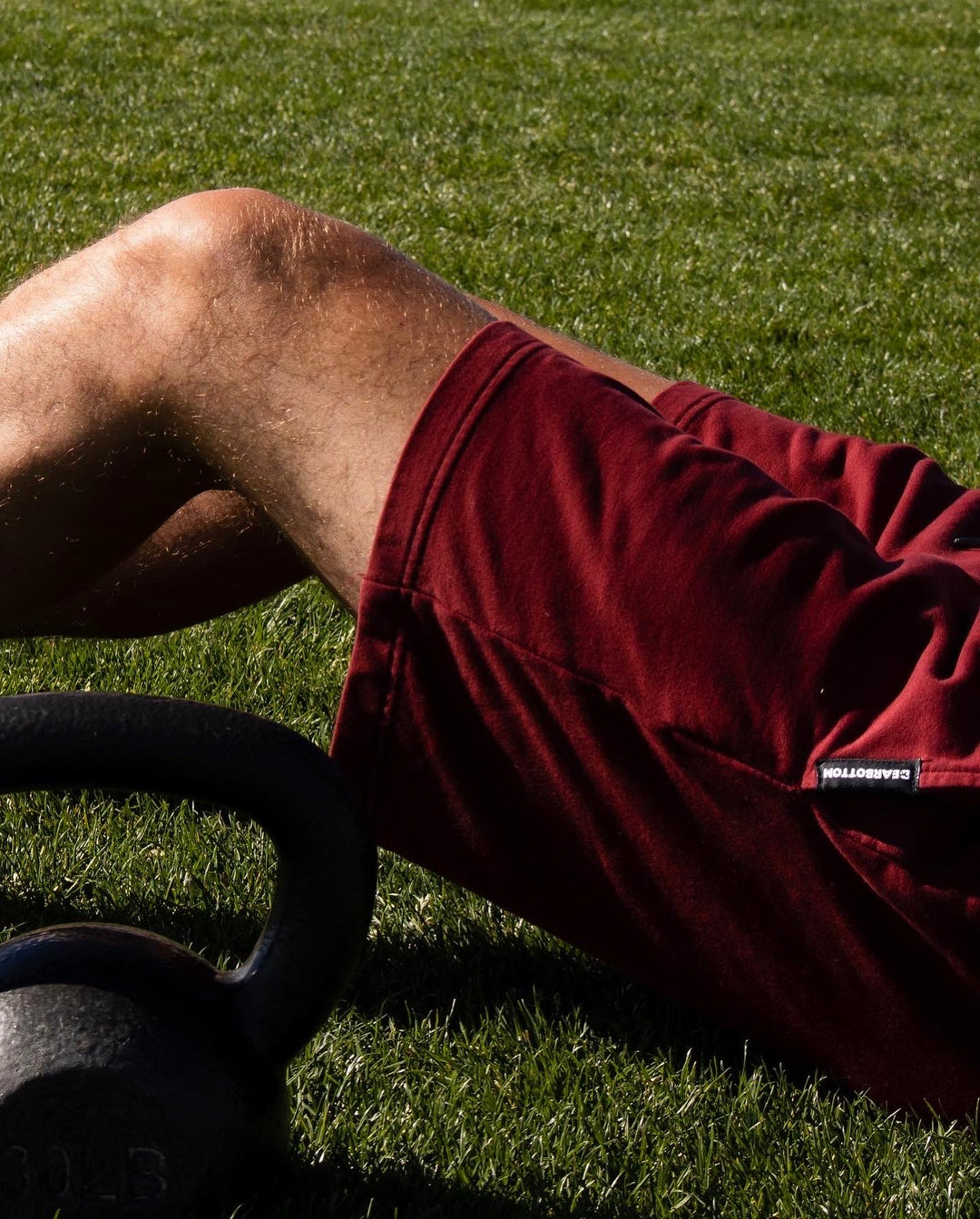 Man's legs sitting in grass wearing Loft Short 7" Maroon