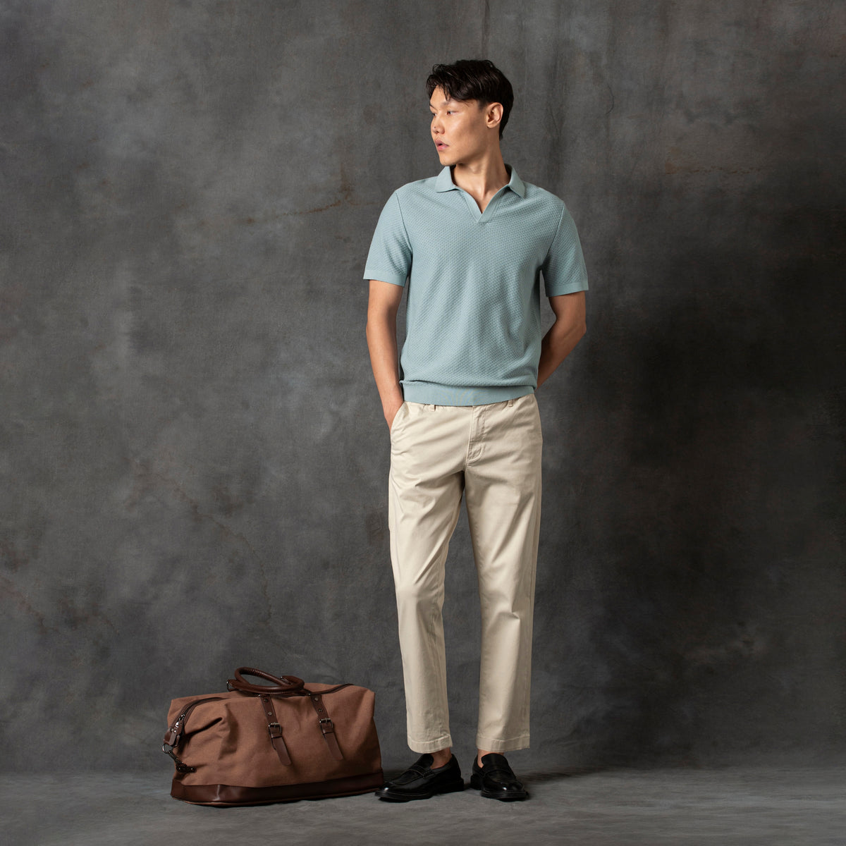 Diamond Knit Sweater Polo Shark charcoal background full body on model with travel duffle