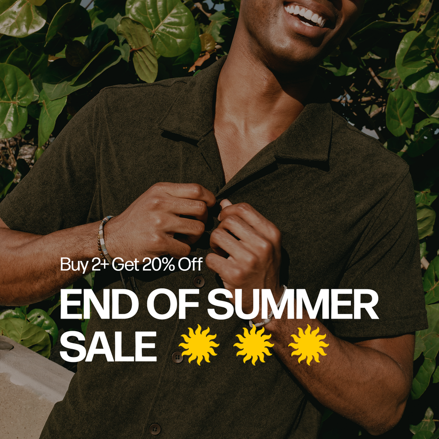 A man wearing a Coastal Terry Shirt Dark Pine stands outdoors in front of dense green foliage, holding the collar open. White promotional text on the right reads 'Buy 2 Get 20% Off END OF SUMMER SALE' with three yellow sun icons below.