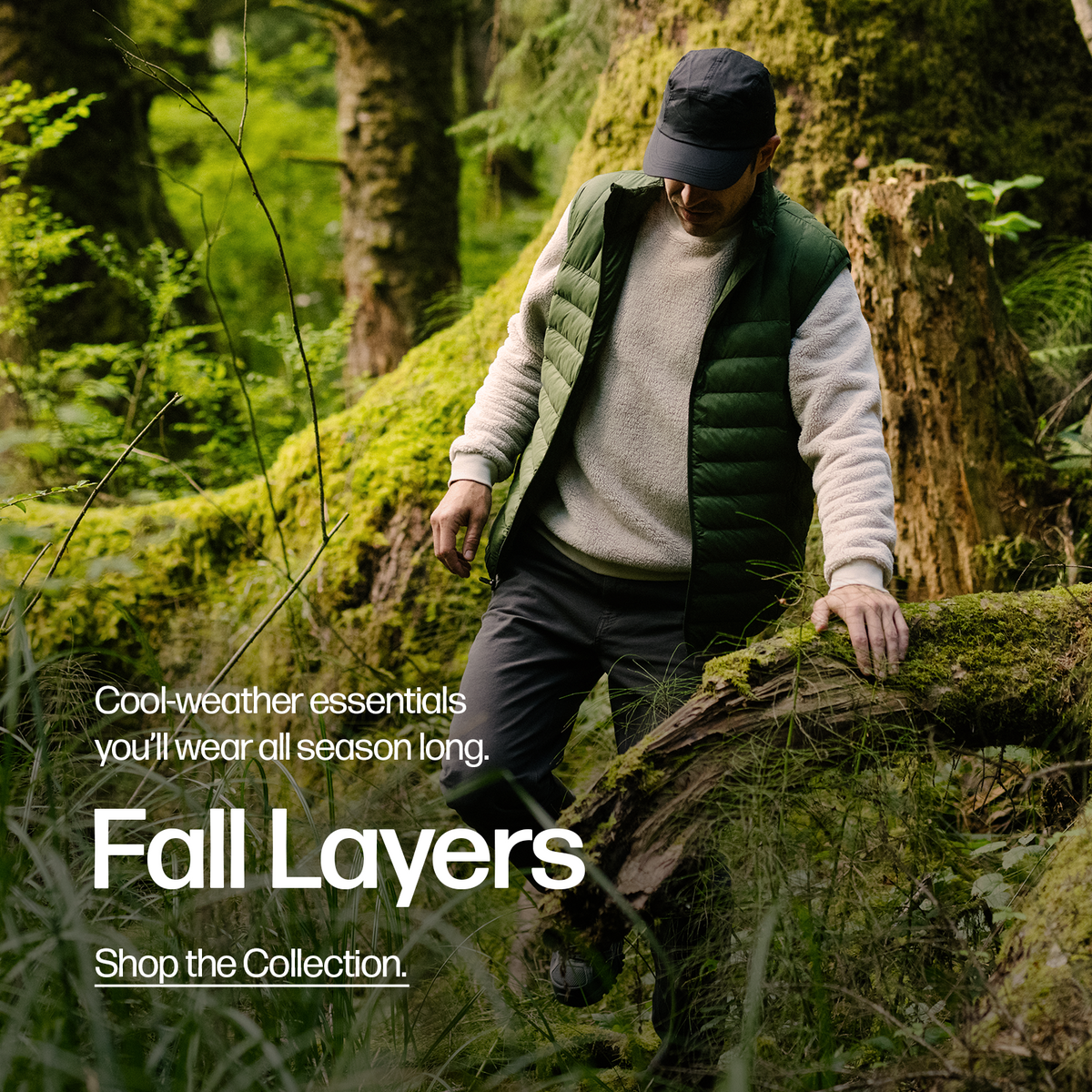 A man outside walking through a forest wearing the Sherpa Crewneck in Bone and the PrimaLoft Packable Vest in Pine Green.