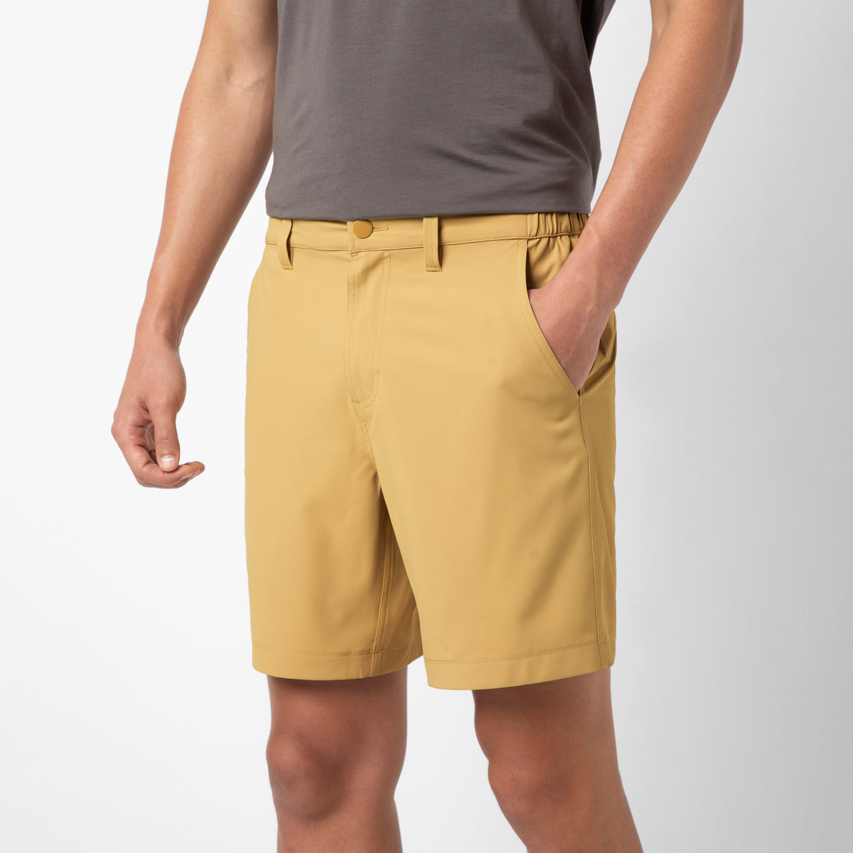 A person wearing a grey t-shirt and mustard yellow Hybrid Short, with hands in pockets, stands against a white background—showcasing the Hybrid Short's travel-ready performance.
