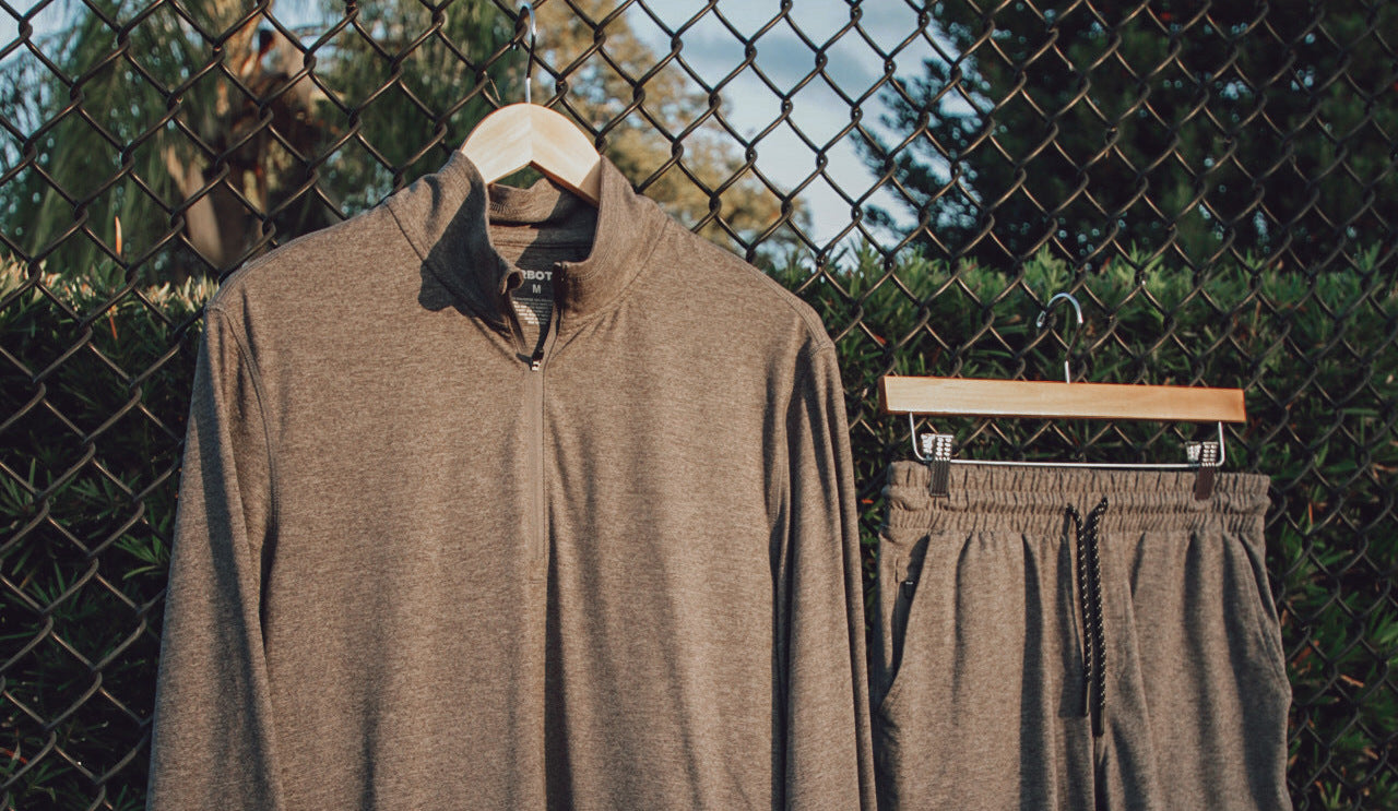 Tech Half-Zip Grey and Tech Short Grey hanging on hangers on fence on tennis court
