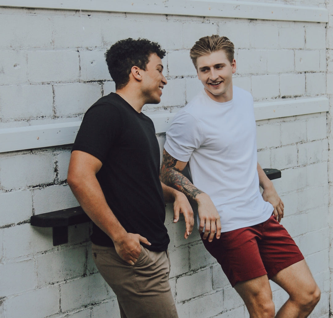 Man in Short Sleeve Tech Tee in Solid Black and Stretch Chino Pants Desert talking to other man wearing Stretch Short 7" in Maroon and Short Sleeve Tech Tee Solid White