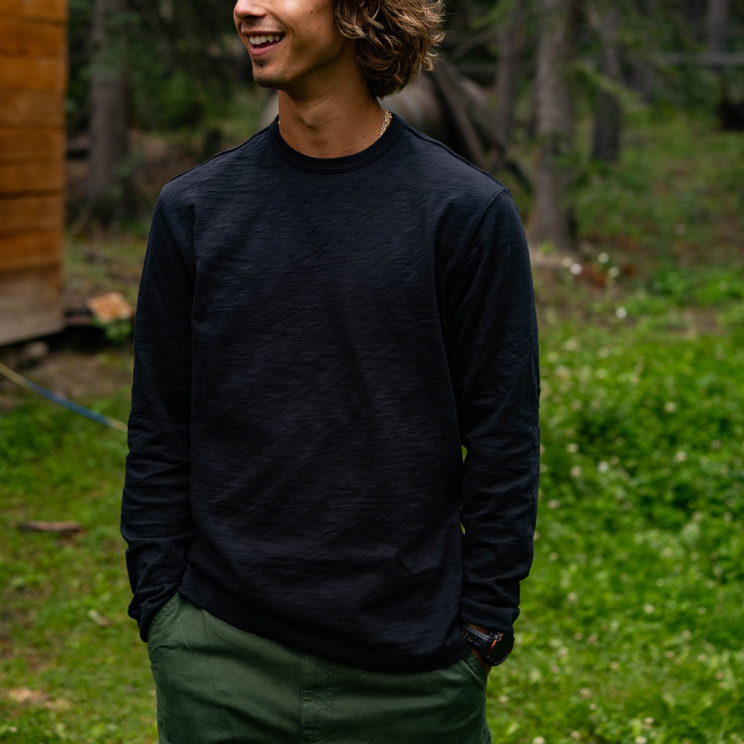 Man wearing a Rugby Crew Black standing in a grassy area with trees in the background.