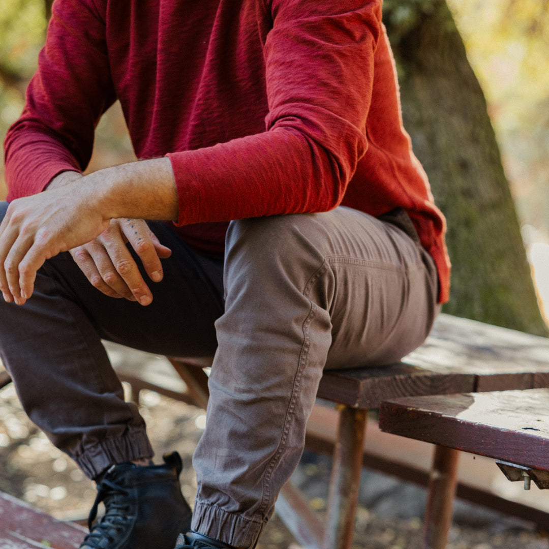 Person wearing a Rugby Crew Crimson sitting on a wooden picnic table outdoors.