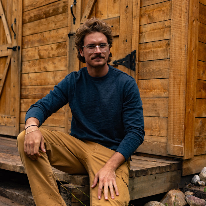 Man sitting on wooden steps in front of a wooden building wearing Rugby Crew Navy