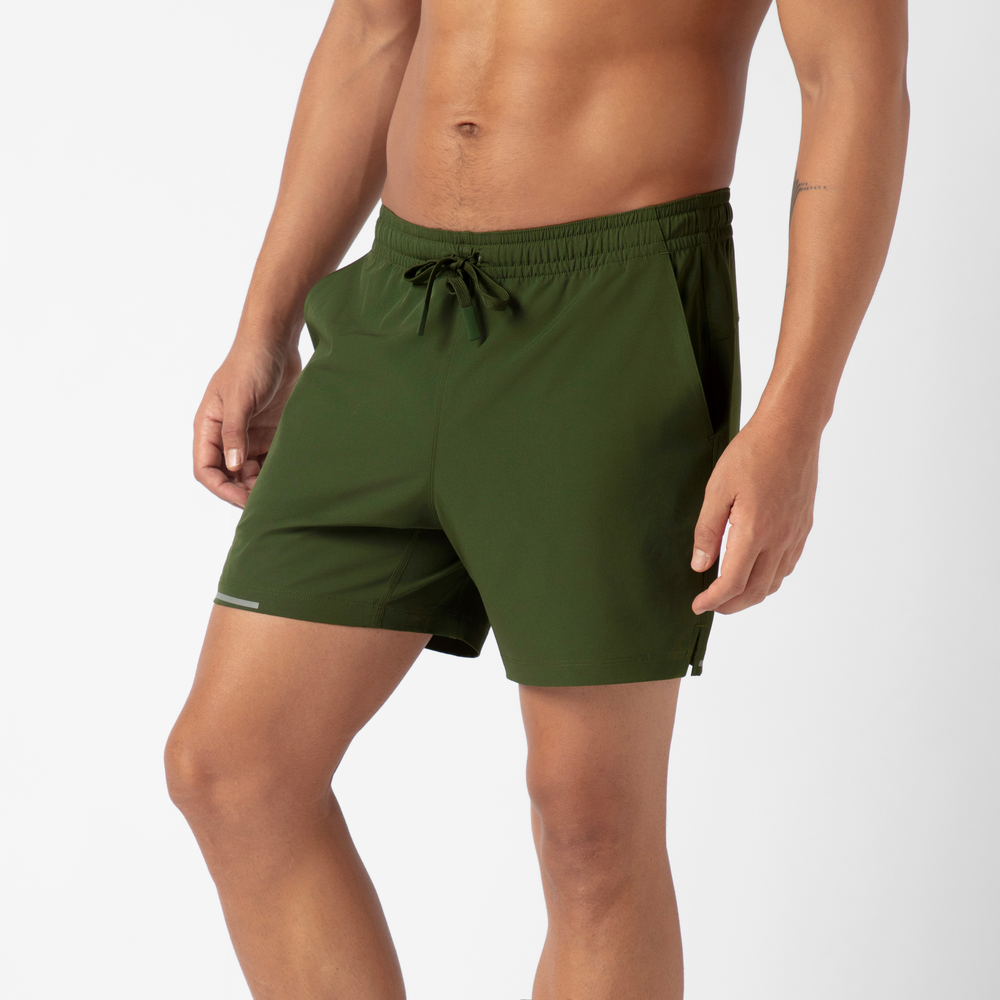 Wearing the Run Short v2 in olive green, a person stands against a white background. These mid-thigh performance shorts are made from recycled polyester, include side pockets and a drawstring waistband, and feature moisture-wicking fabric.