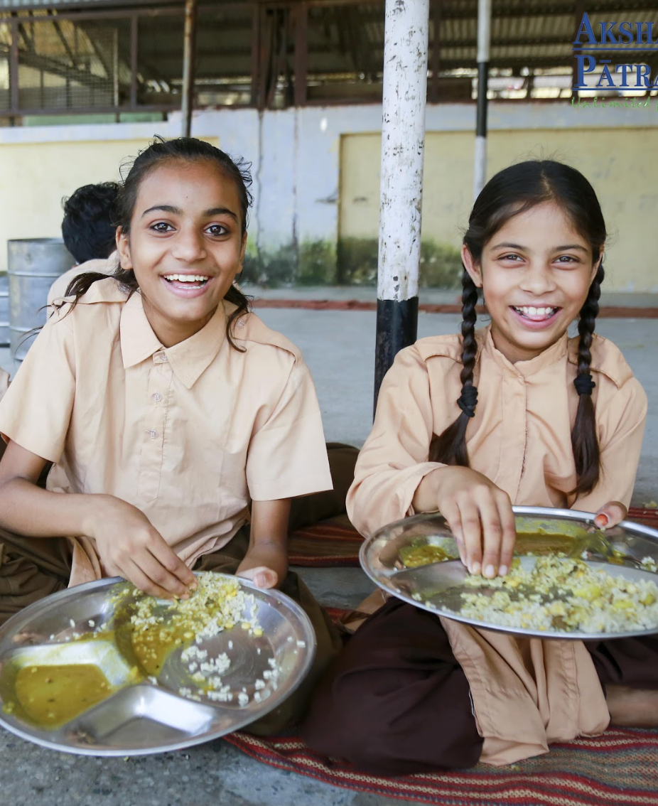 Two girls in India at school eating lunch and smiling