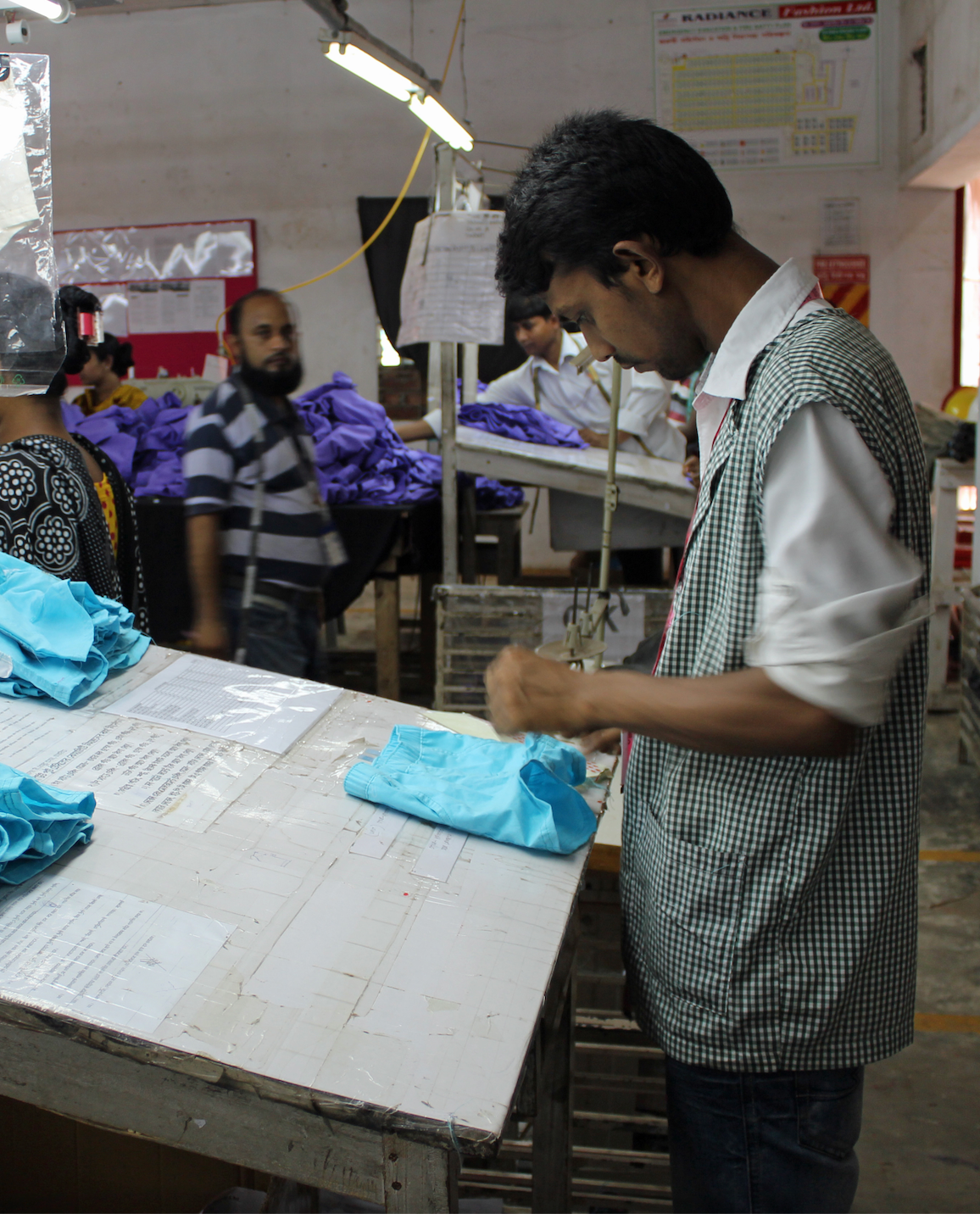 Garment worker inspecting pair of bright blue shorts for donations in Bangladesh