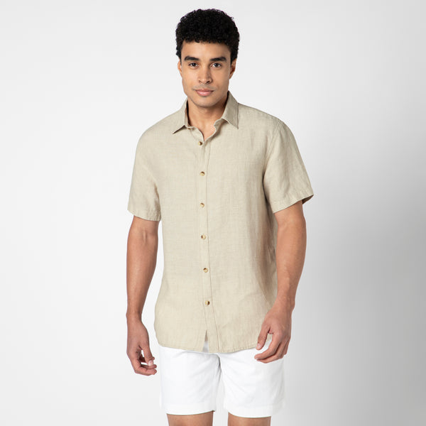 A man in a stone Linen Short Sleeve Shirt and white shorts stands against a plain white background, looking at the camera with a neutral expression to showcase natural comfort and effortless style.
