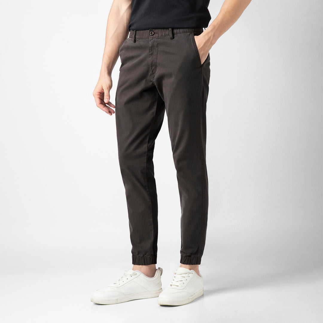 A person stands at an angle in the Coal Stretch Jogger with one hand tucked into the side pocket, wearing a black tee and white sneakers against a plain light grey background.