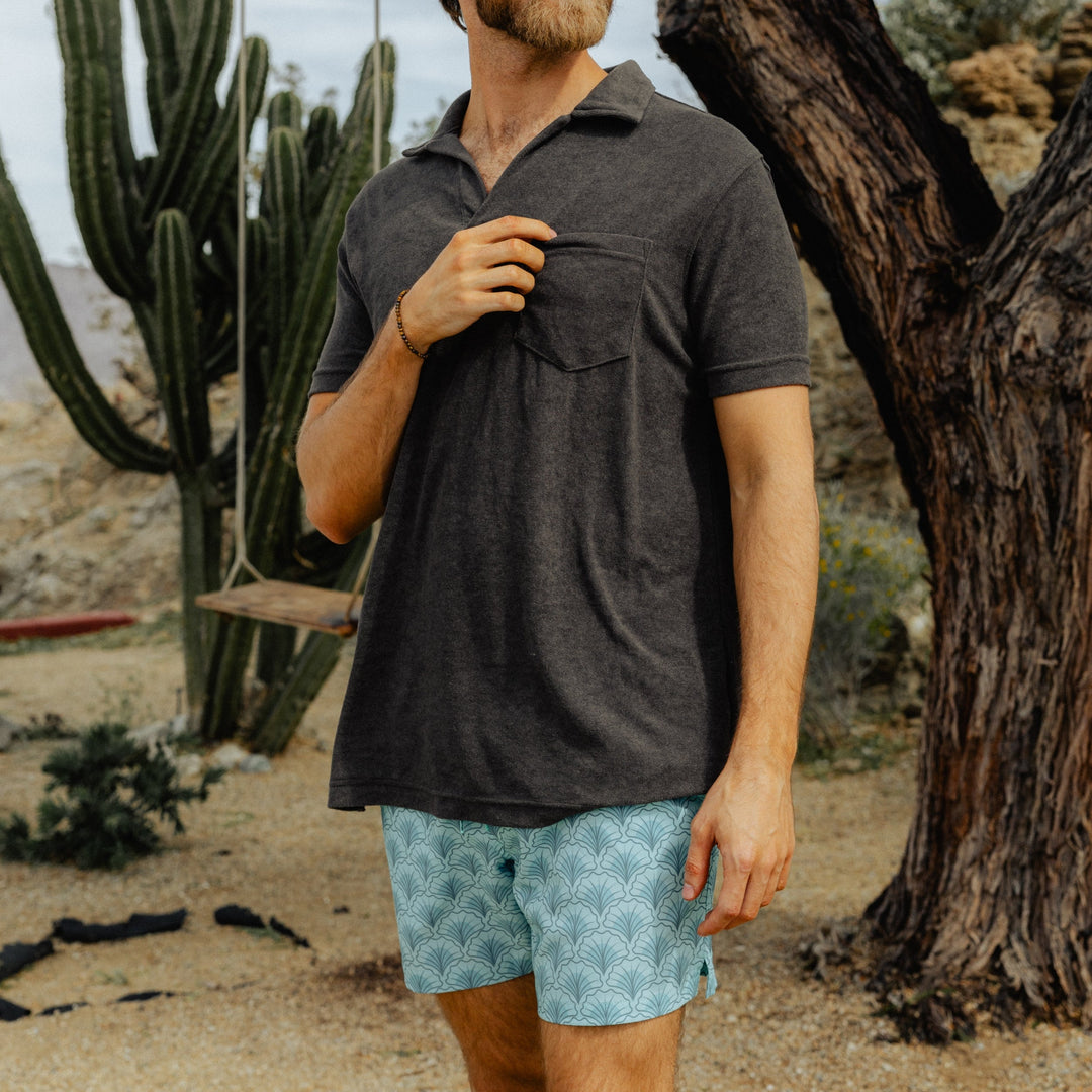 A man wears the Stretch Swim Trunk (Clearance) in Shell, 5.5" inseam, with a dark grey Coastal Terry Polo, standing in front of a cactus.