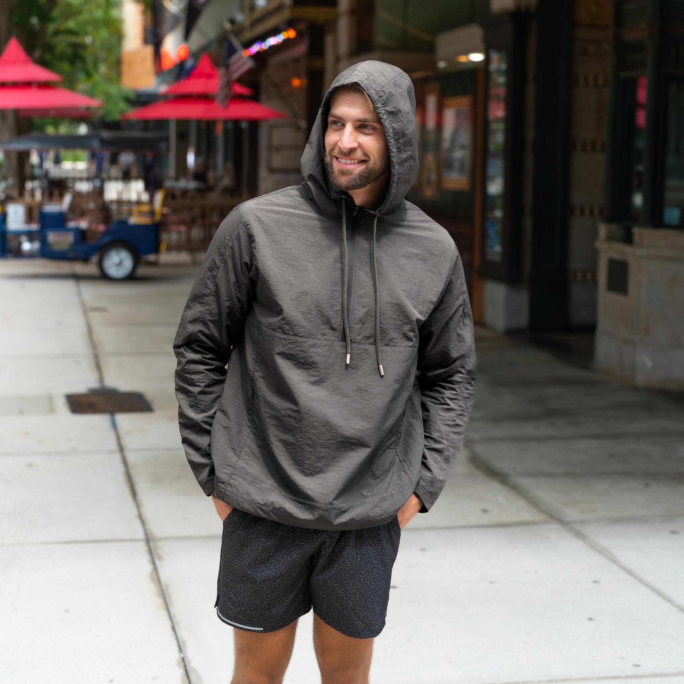 Windbreaker Jacket in Graphite grey front on model wearing hood in a downtown setting worn with Run Short v2 in Carbon Black