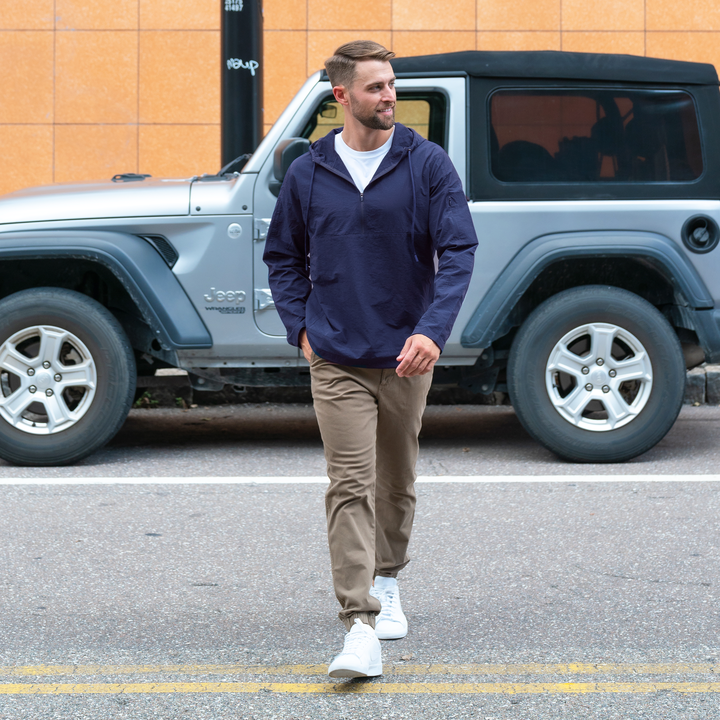 Windbreaker Jacket in Navy blue on model walking across the street in front of a grey Jeep worn with Stretch Jogger in Desert