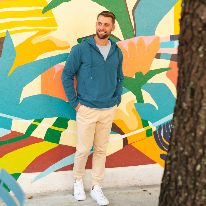 Windbreaker Jacket in Ocean blue on model standing outside in front of brightly colored wall worn with Stretch Jogger in Sand Dune