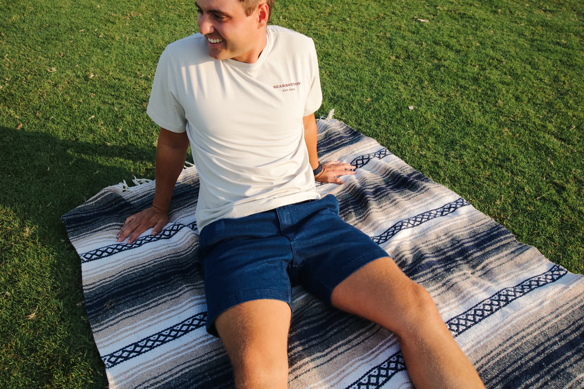 A man sitting comfortably on a striped Mexican blanket, legs extended, wearing dark wash Stretch Denim Short