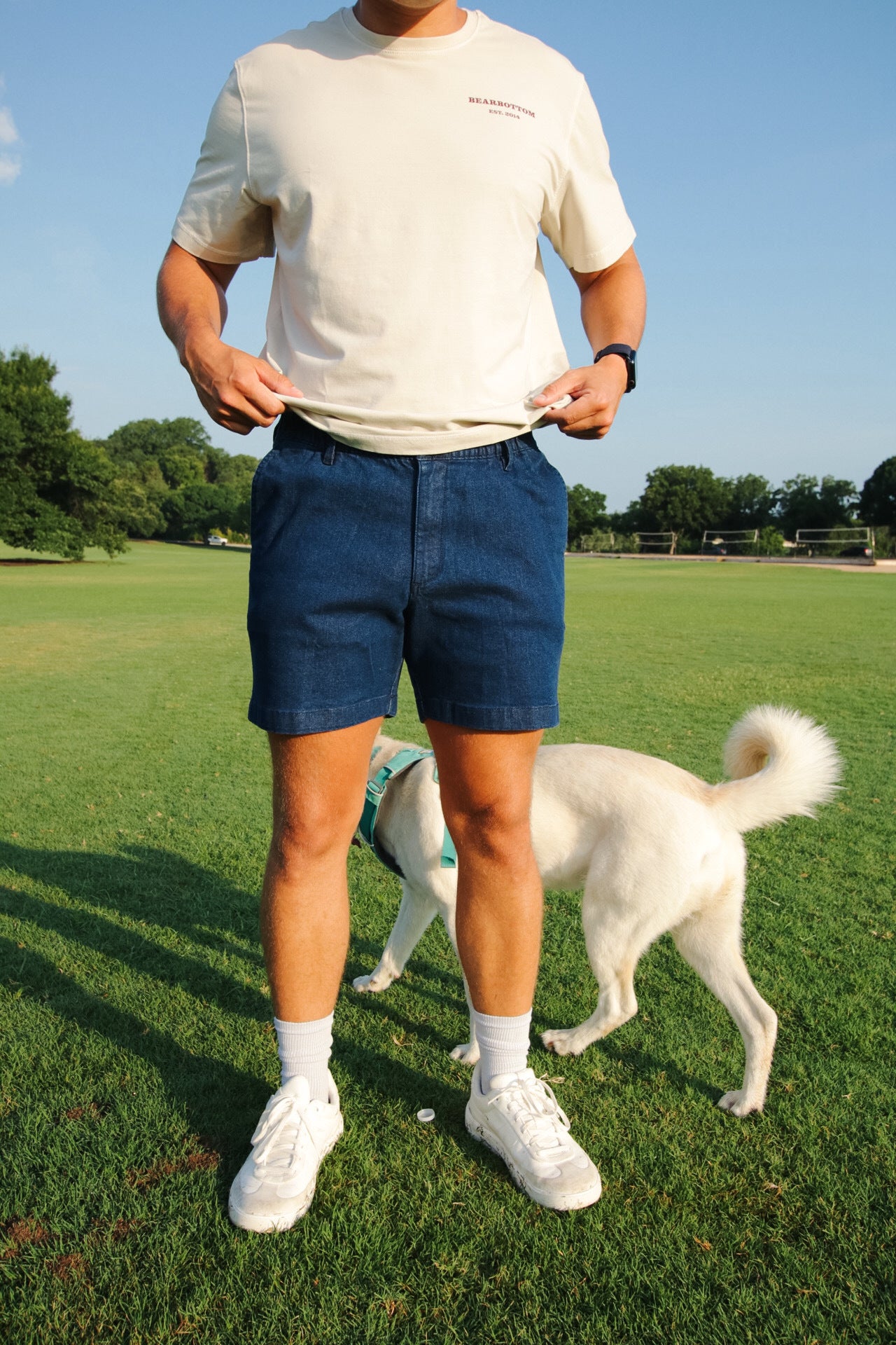 A man standing on grass wearing dark wash Stretch Denim Short, showing the 5.5 inch inseam length above the knee
